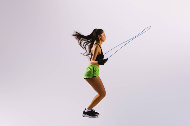 Fit young woman skipping rope. Portrait of muscular young woman exercising with jumping rope on grey white background. - Photo, Image