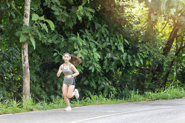 Mladá žena běžec poslech hudby na sluchátka při běhu na silnici v dopoledních hodinách. - Fotografie, Obrázek