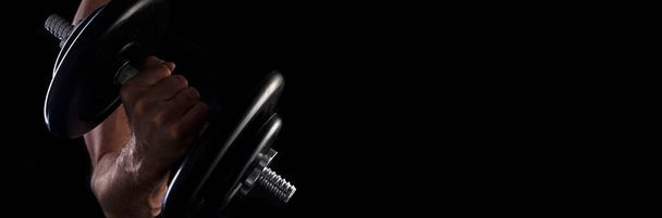 Man's hand with metal dumbbell on dark background with place for text. - 写真・画像