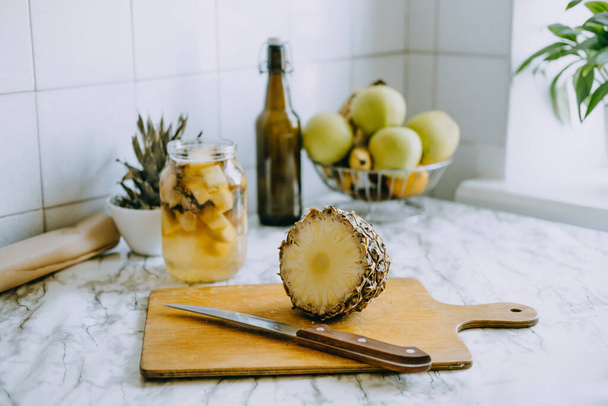 Fermented pineapple kombucha drink tepache. Cooking process of homemade probiotic superfood pineapple beverage. Drink jar and sliced pineapple on home kitchen - Foto, Imagen