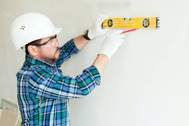Hombre reparador aplica un nivel a la pared - Foto, Imagen