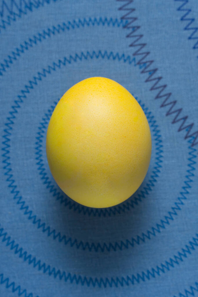 Huevo amarillo de Pascua sobre un fondo azul con un patrón - Foto, Imagen