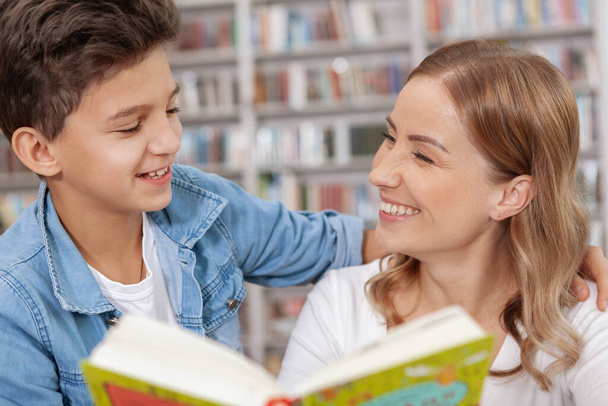 Close up of a happy young boy and hid mother laughing while reading a book together - Foto, Bild