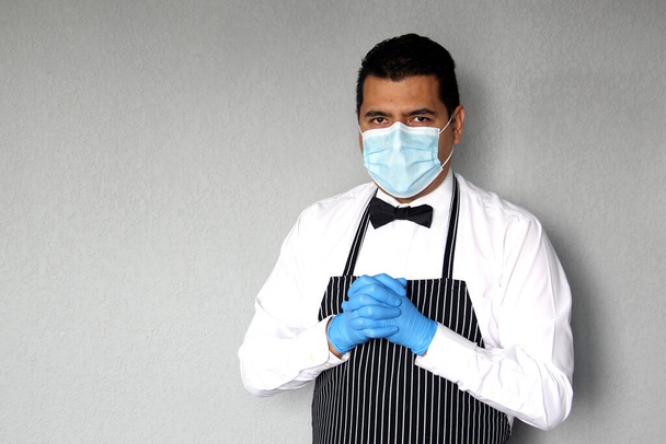 Latino σερβιτόρος άνθρωπος με προστατευτική μάσκα, λειτουργεί με γάντια λάτεξ, νέα κανονική σε εστιατόρια. κοβίδιο-19 - Φωτογραφία, εικόνα