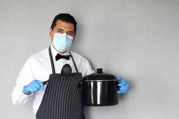 Latino chef with kitchen utensils working with mouth mask and latex gloves, new normal for the covid-19 virus - Photo, image