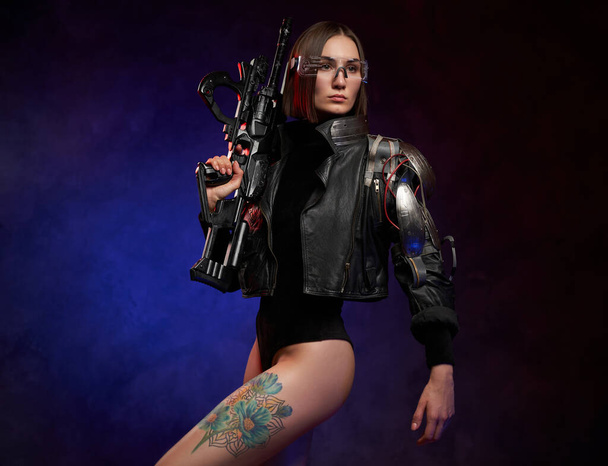Karanlık ve atmosferik stüdyoda elinde tüfek tutan gelecekçi siber kadın. - Fotoğraf, Görsel