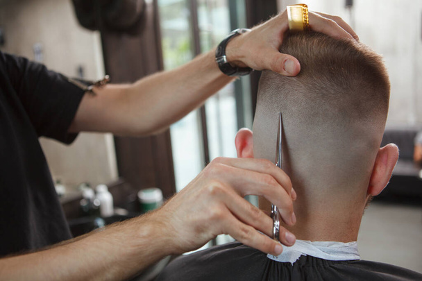Close up rear view shot of a hairstylist using scissors, cutting hair of male client - Foto, imagen