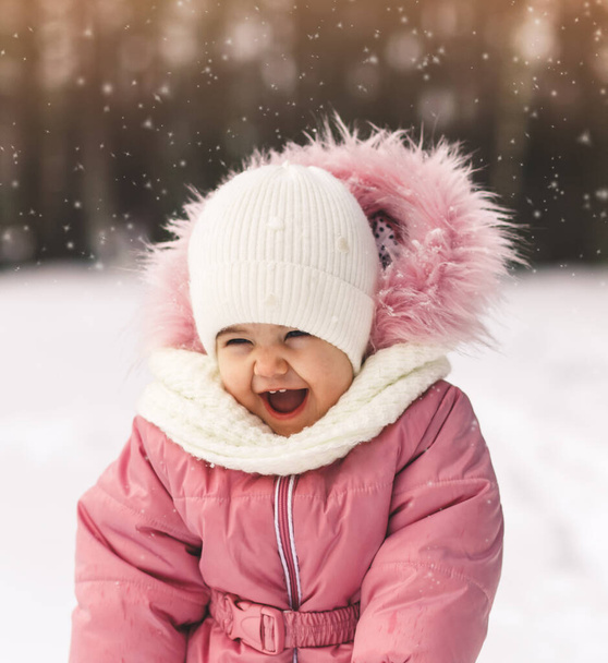 Μικρό χαριτωμένο κορίτσι γελάει σε ένα χιονισμένο πάρκο το χειμώνα - Φωτογραφία, εικόνα