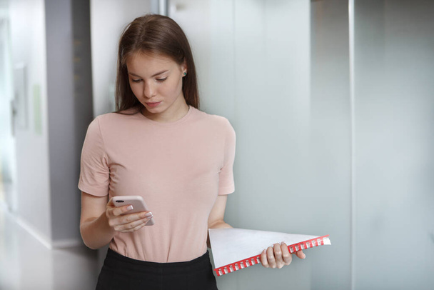 Attractive female entrepreneur using her smart phone while walking corridor at workplace - Photo, Image