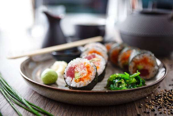 Sushi maki rola com atum, caviar de peixe voador, caranguejo, abacate em um prato com pauzinhos, molho de soja, wasabi e gengibre. Japonês tradicional comida closeup servido para o almoço no moderno restaurante gourmet. - Foto, Imagem