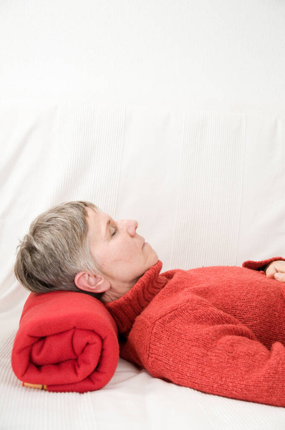 Vue de profil d'une femme âgée allongée sur le dos sur un canapé blanc les yeux fermés ; orientation verticale.  - Photo, image