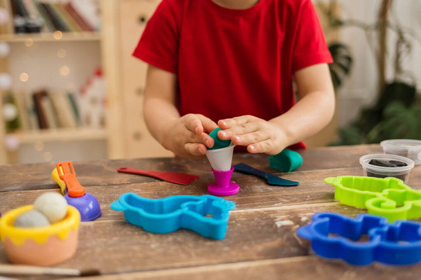 close-up of a child playing with plasticine and plasticine molds on a wooden table. Child development - Foto, afbeelding