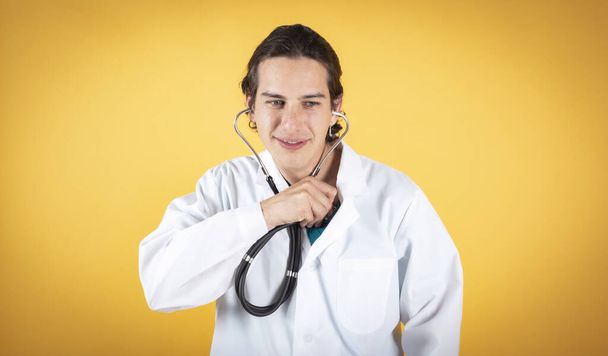 médico bonito com o próprio estetoscópio, sorrindo piadas, fundo amarelo, espaço de cópia - Foto, Imagem