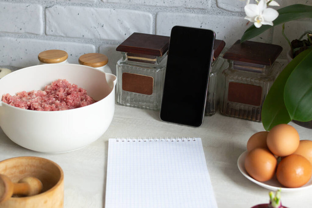 Online cooking courses. The smartphone is in the home kitchen among the products. Lesson on cooking a meat dish. Copy space. - Fotoğraf, Görsel