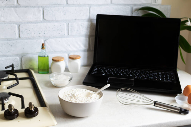 Online főzőtanfolyamok. A laptop az otthoni konyhában van a termékek között. Lecke a lisztétel főzéséről. Fénymásolási hely. - Fotó, kép
