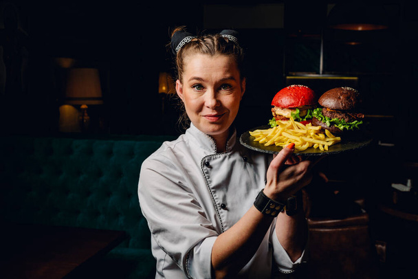 young woman chef with two burger on dark background in cafe - Foto, Bild