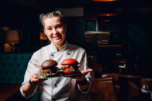 young woman chef with two burger on dark background in cafe - Фото, зображення