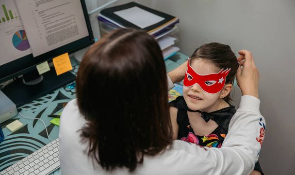 Woman teleworking and putting costume mask on her daughter - Photo, Image