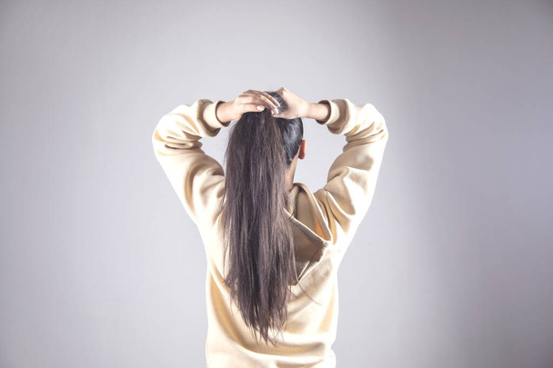 young woman to tie hair on grey background - Zdjęcie, obraz