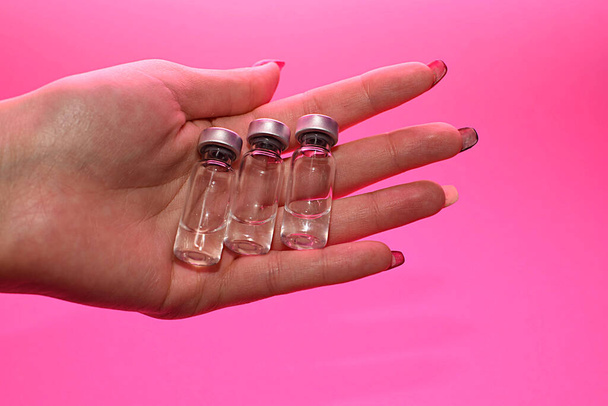 tři ampulky s léky nebo vakcinace v rukou na růžovém pozadí. koncepce humánní a veterinární medicíny - Fotografie, Obrázek