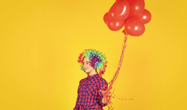 valentines day party. child wear rainbow wig hair yellow background. happy kid hold party balloons. heart balloons for love day. surprise for valentine. colorful and bright. small girl in periwig - 写真・画像