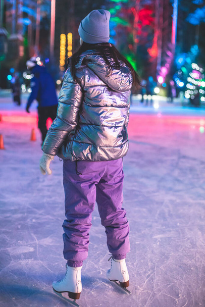 Girl ice skating on the ice rink arena with happy people around, concept of ice skating in winter, winter activities, holiday christmas time, with a new year decoration and illumination - Photo, image