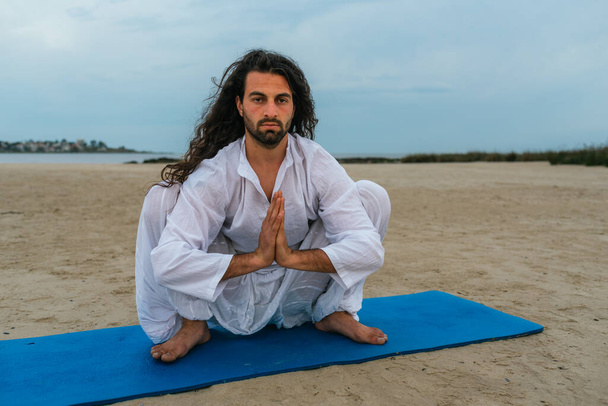 Stock fotó felnőtt férfi hosszú haj csinál jóga pózok a strandon. - Fotó, kép
