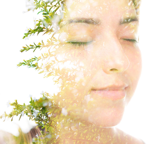 A double exposure portrait of a young beautiful brunette with her eyes closed and branches with little green leaves - Foto, immagini