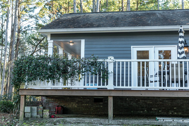 Lado de la pequeña casa móvil gris azul con un porche frontal y lateral con barandilla blanca - Foto, Imagen