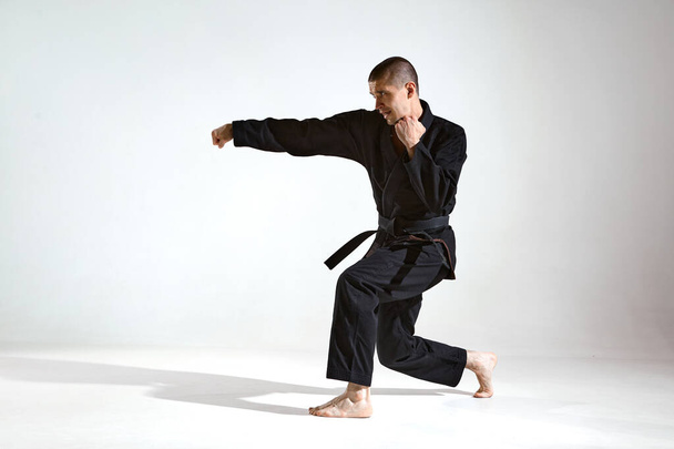 Peleador en kimono negro que demuestra la técnica de karate en el fondo del estudio con espacio de copia - Foto, imagen