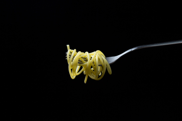 Spaghetti on a black background. Boiled spaghetti on a fork. Isolated spaghetti - Photo, Image