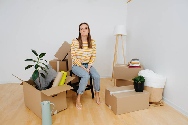 Нове житло, дівчина сидить у кімнаті серед коробки речей
 - Фото, зображення
