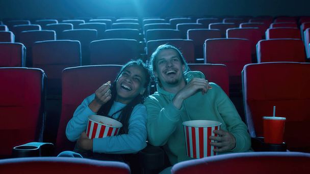Couple of friends sitting at the cinema, watching a movie and eating popcorn - Foto, Bild
