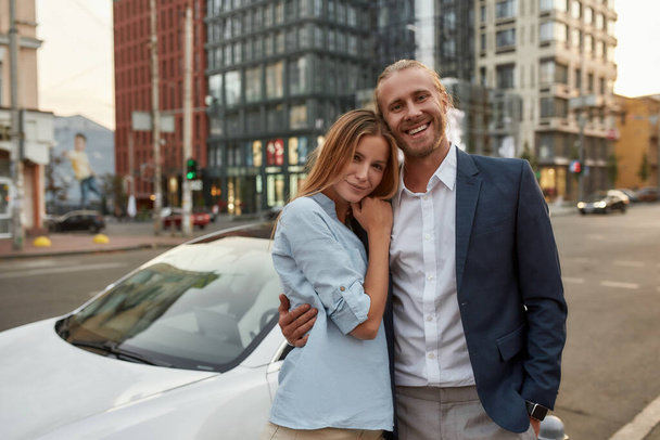 Cheerful caucasian businessman hugging young woman near luxury car - Foto, Imagen