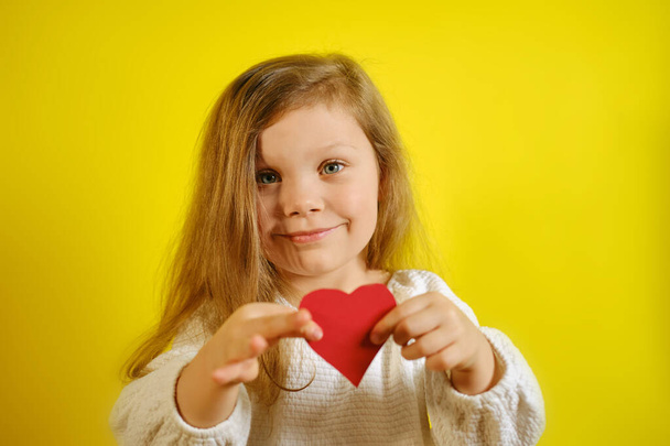 Portré egy kislányról, aki piros szívet tart neked, sárga háttérrel és fénymásoló hellyel. V2. - Fotó, kép