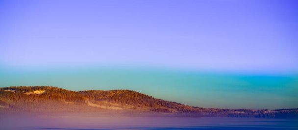 Belo panorama de inverno nevado sobre um lago congelado coberto de neve pesada e uma névoa congelada pendurada em um céu colorido à noite. Foto de alta qualidade - Foto, Imagem