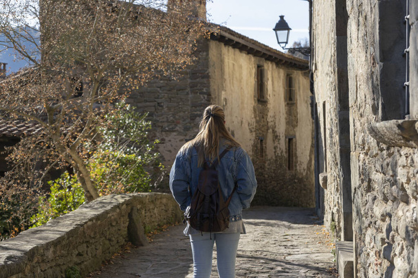 Achteraanzicht van een toeristische vrouw die wandelt in het geweldige oude dorp Rupit in Barcelona, Spanje.Reisbestemming, vakantie en vakantie lifestyle concept. - Foto, afbeelding