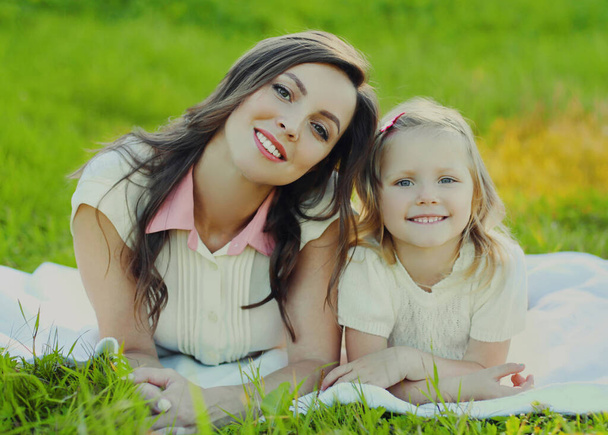 Portrait of happy smiling mother and child lying together on a green grass in summer park - Foto, Imagen
