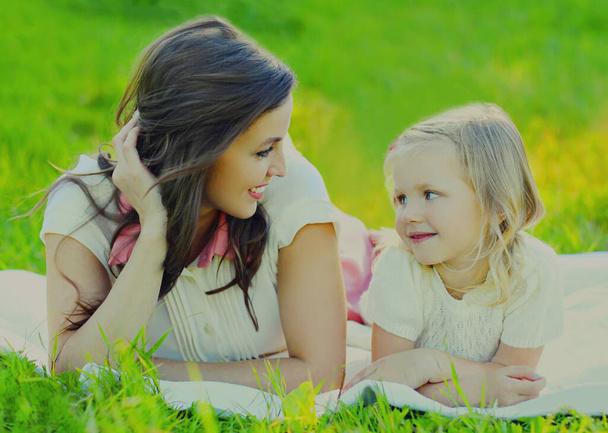 Portrait of happy smiling mother and child lying together on a green grass in summer park - Foto, Imagen