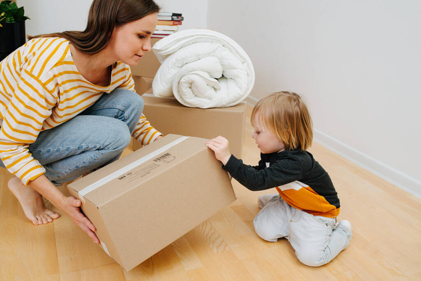 Toddler helps mom open a box after moving into a new home - Fotografie, Obrázek