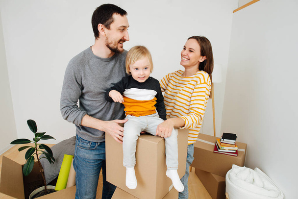 happy young family in new house among boxes amid white walls - Valokuva, kuva