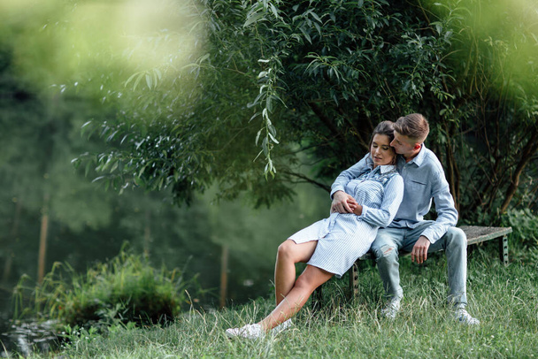 Ein junges Paar sitzt an einem sonnigen Tag in der Nähe des Sees und umarmt sich. Mann und Frau im Sommerurlaub. Konzept der schönen Familie. Selektiver Fokus. - Foto, Bild