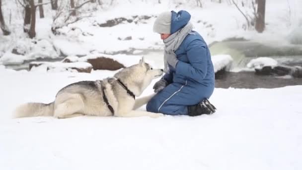 Blanke vrouw traint Snowy Siberische husky hond in de winter. Rivieroever. - Video