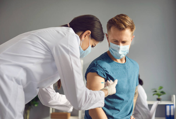 Молодая женщина-врач в медицинской маске вводит вакцину против инфекции 19-Ncov для пациента мужчины - Фото, изображение