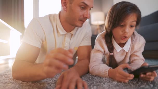 Vater und Tochter genießen die gemeinsame Zeit und nutzen ein Tablet zur Familienunterhaltung, während sie zu Hause im Wohnzimmer auf dem Boden liegen. - Filmmaterial, Video