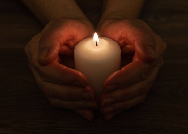 Eine weiße Kerze brennt im Dunkeln. Eine Kerze umgeben von Händen. - Foto, Bild