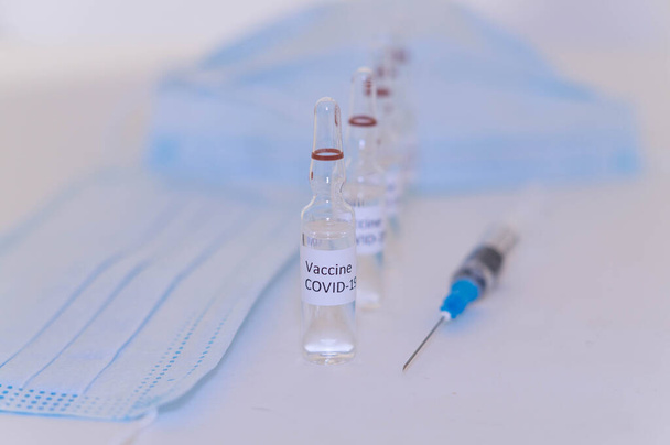Covid-19 vakcinával ellátott ampullák az asztalon lévő laboratóriumon, fecskendő és maszk a háttérben - Fotó, kép