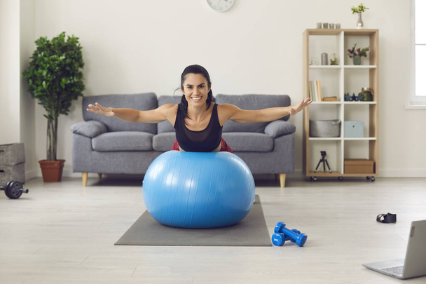 Portrait of a smiling athletic woman lying on a fitness ball with her arms outstretched. - Фото, зображення