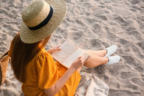 Young woman reading book on sandy beach, back view - Foto, imagen