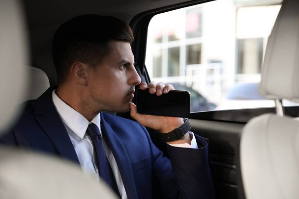 Beau homme avec smartphone sur le siège arrière de la voiture moderne - Photo, image